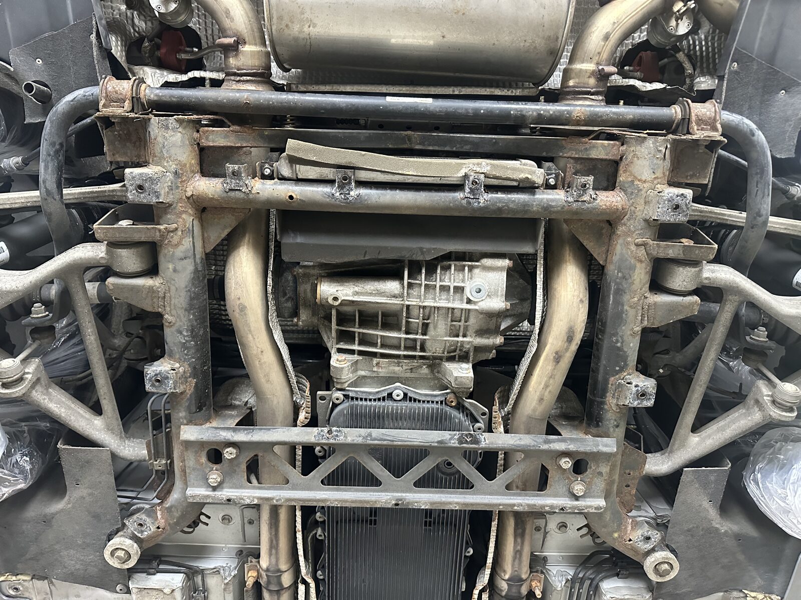 Before – surface corrosion – The rear subframe on arrival: surface corrosion across the crossmember, brackets and anti-roll bar, with the original coating starting to lift and fail.