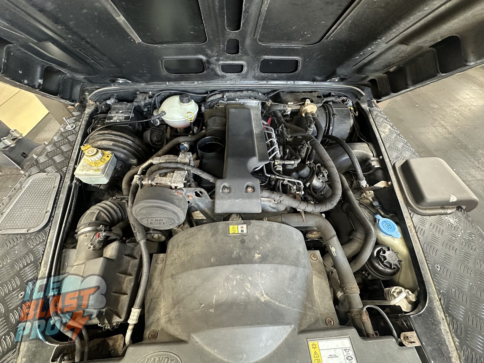 Land Rover Defender 90 engine bay before cleaning, with dust and dry grime over the engine cover, hoses and ancillaries
