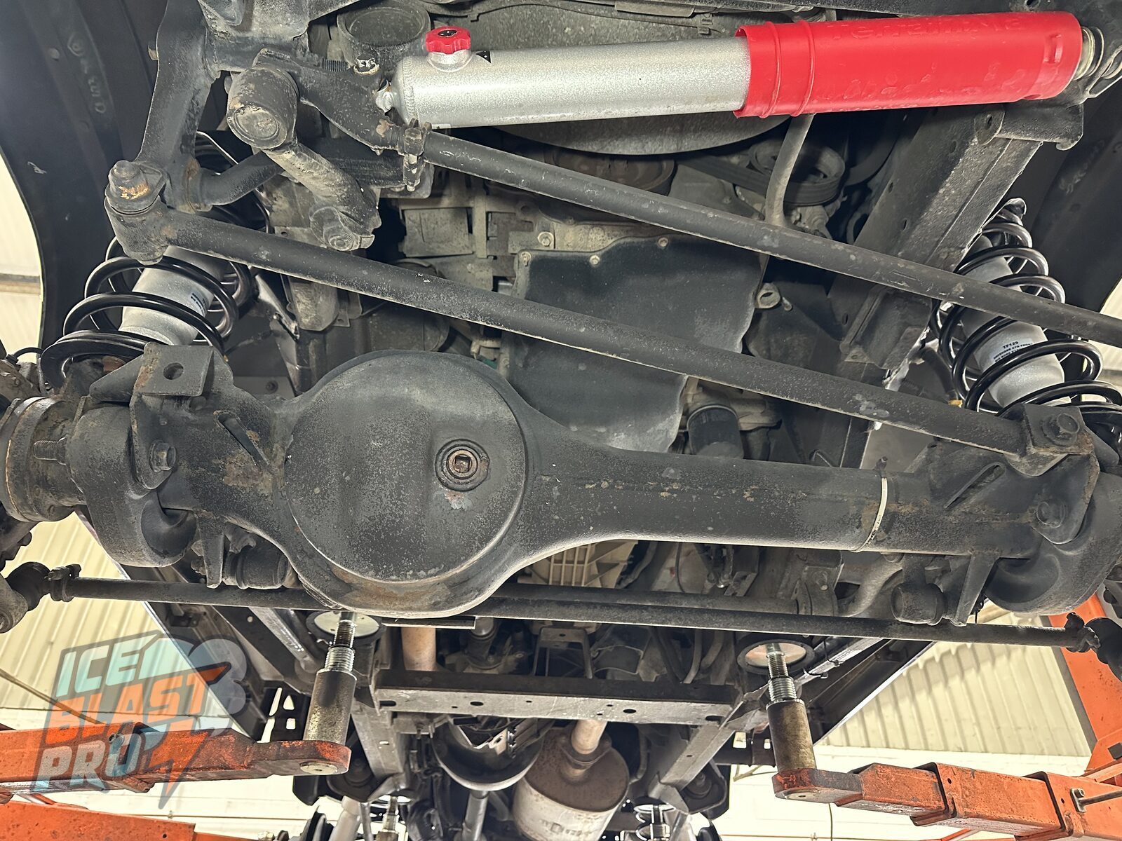Front axle & diff – Surface corrosion across the front axle, differential housing and radius arms, with road dirt packed into the seams where moisture sits.