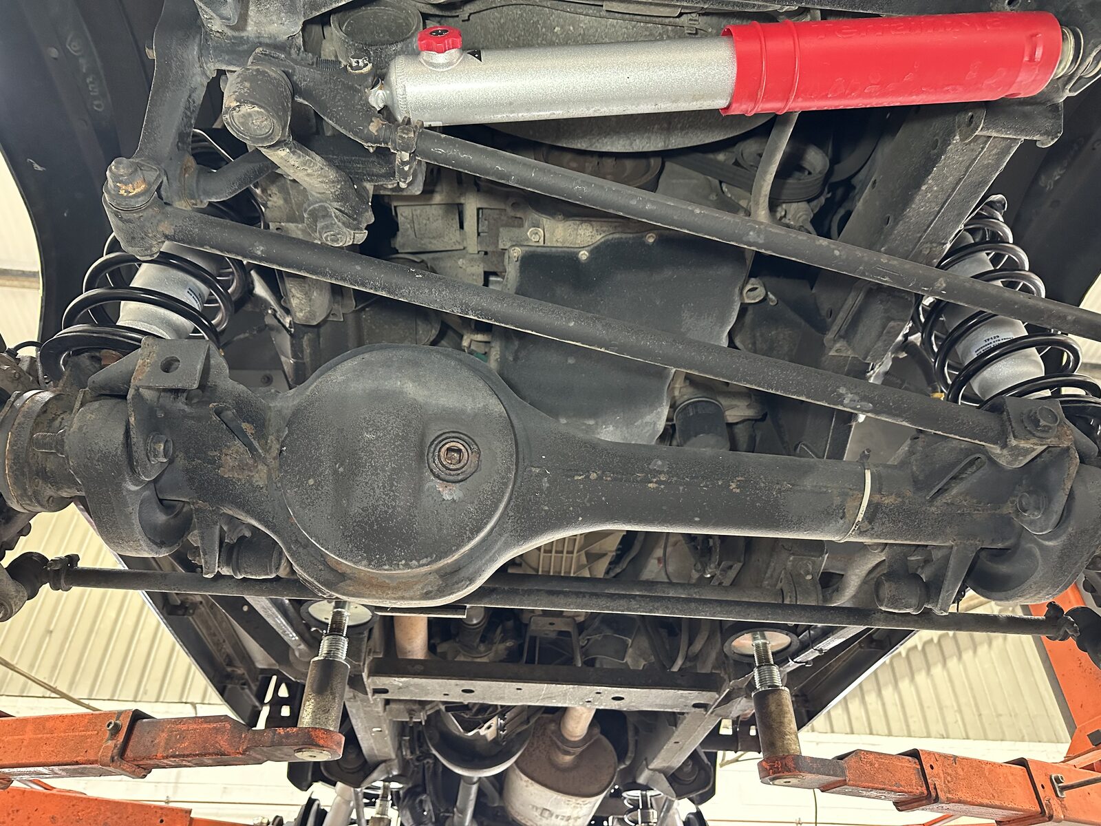 Front axle & diff – Surface corrosion across the front axle, differential housing and radius arms, with road dirt packed into the seams where moisture sits.