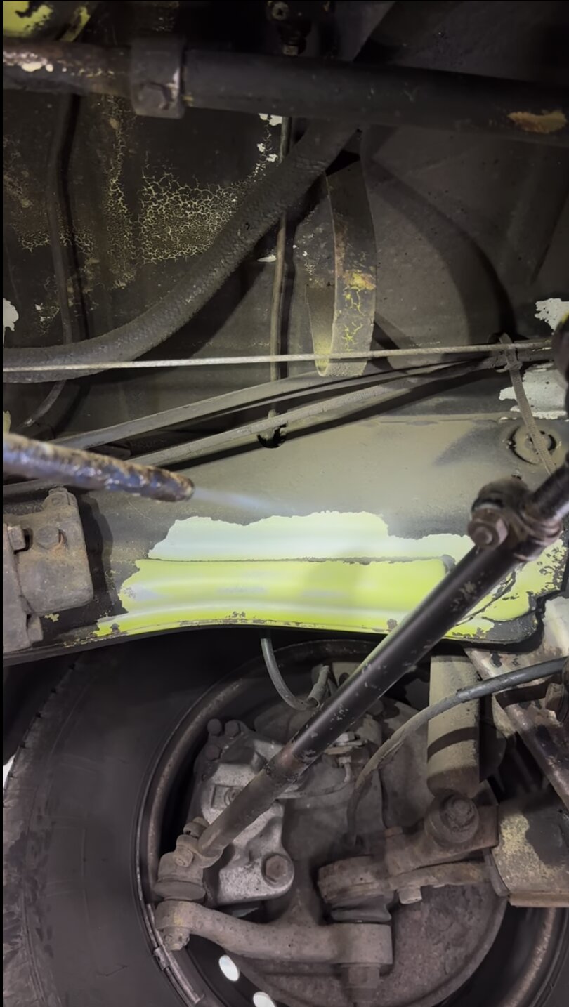 Dry ice blasting a car underbody, the jet stripping grime from a chassis member to reveal the original factory paint beneath while leaving the surrounding suspension and brake parts untouched.