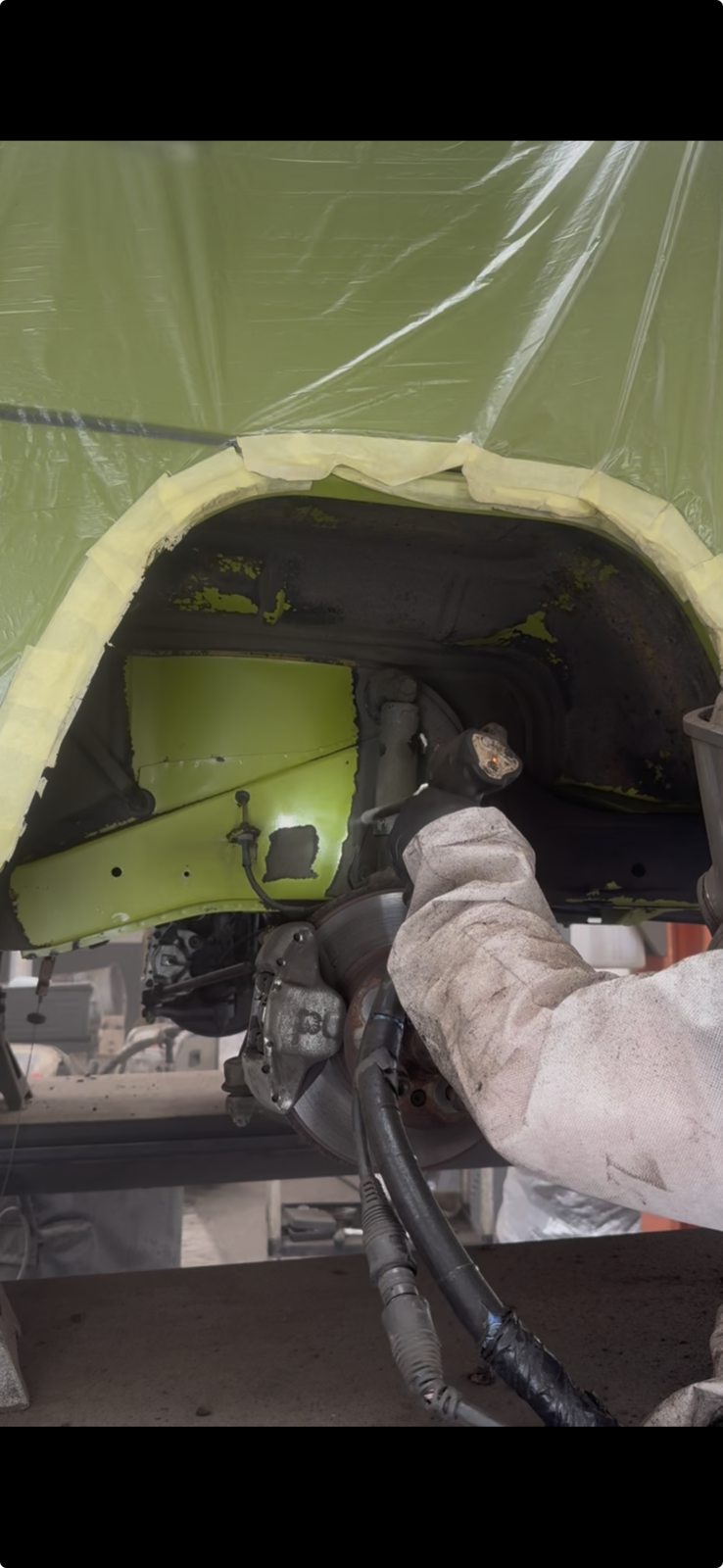 A wheel arch being dry ice blasted with the bodywork wrapped, the painted edge masked off and the operator in protective workwear and gloves.