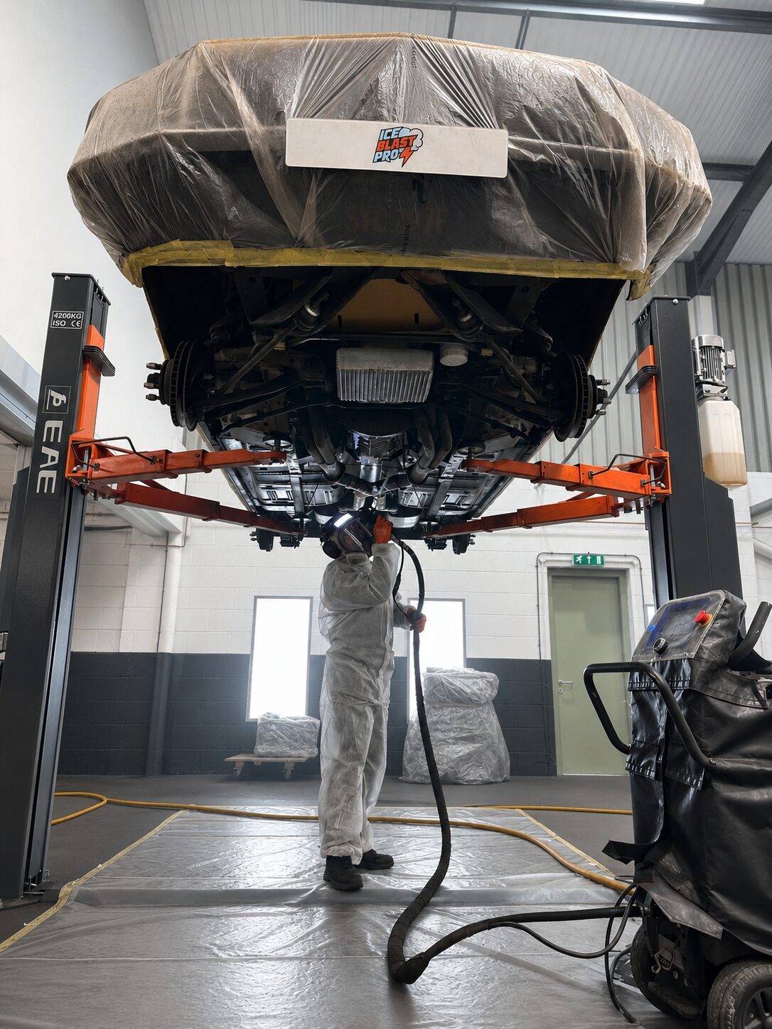 A Ford Mustang wrapped and raised on a two-post lift while a technician dry ice blasts its underbody at IceBlastPro