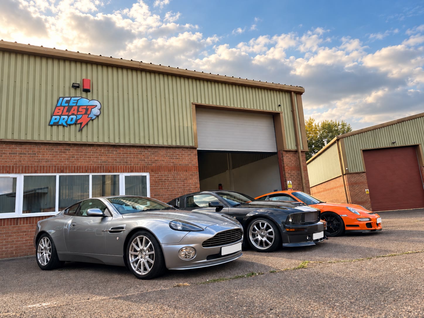 Outside the IceBlastPro workshop in Oxfordshire – an Aston Martin, Ford Mustang and orange Porsche lined up beneath the workshop sign