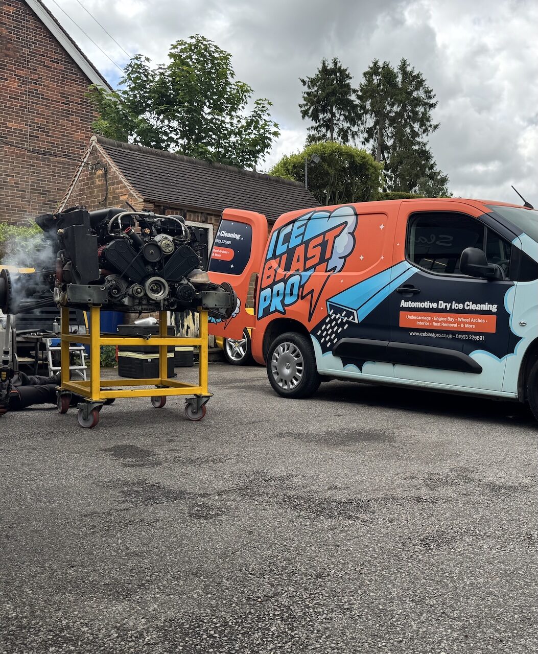 A removed engine on a wheeled stand on a workshop forecourt, with two branded IceBlastPro dry ice cleaning vans behind