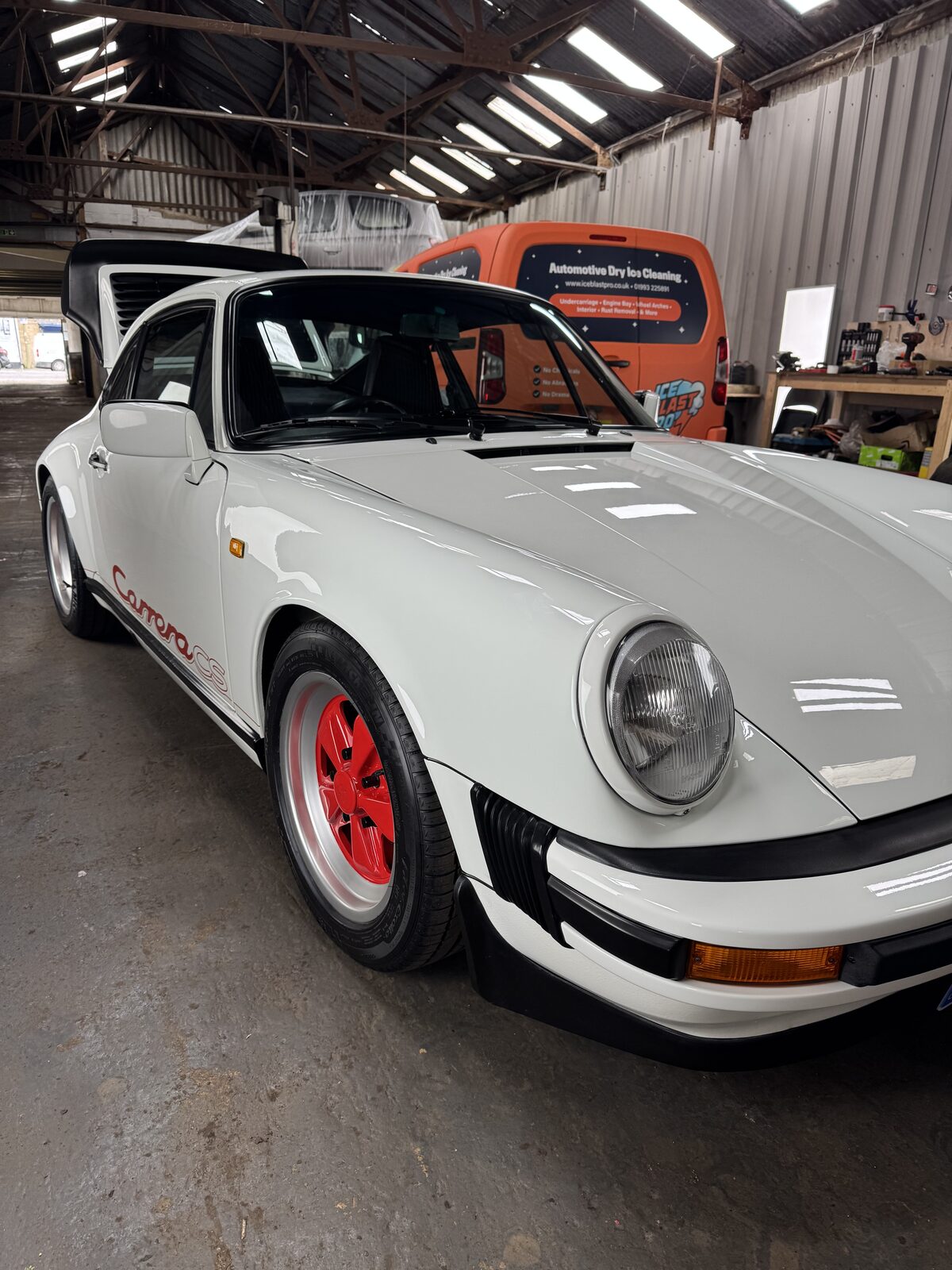 White Porsche 911 Carrera CS with red wheels in the IceBlastPro workshop, in for engine bay dry ice cleaning before a concours event