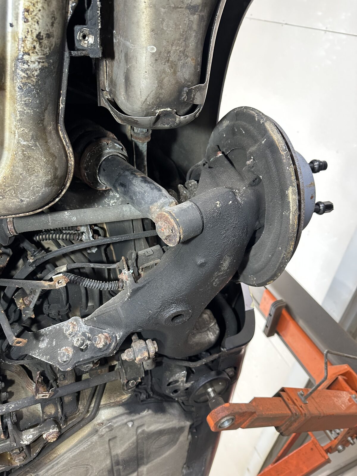 Porsche 911 Carrera 4 rear lower suspension arm before treatment – the alloy arm grimy beneath the exhaust