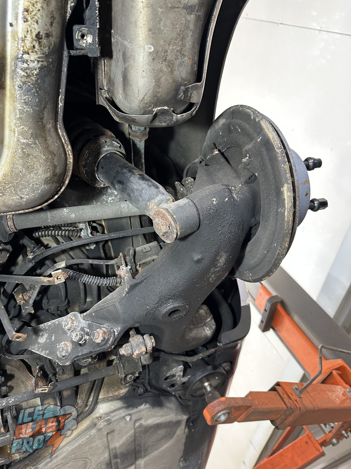 Porsche 911 Carrera 4 rear lower suspension arm before treatment – the alloy arm grimy beneath the exhaust