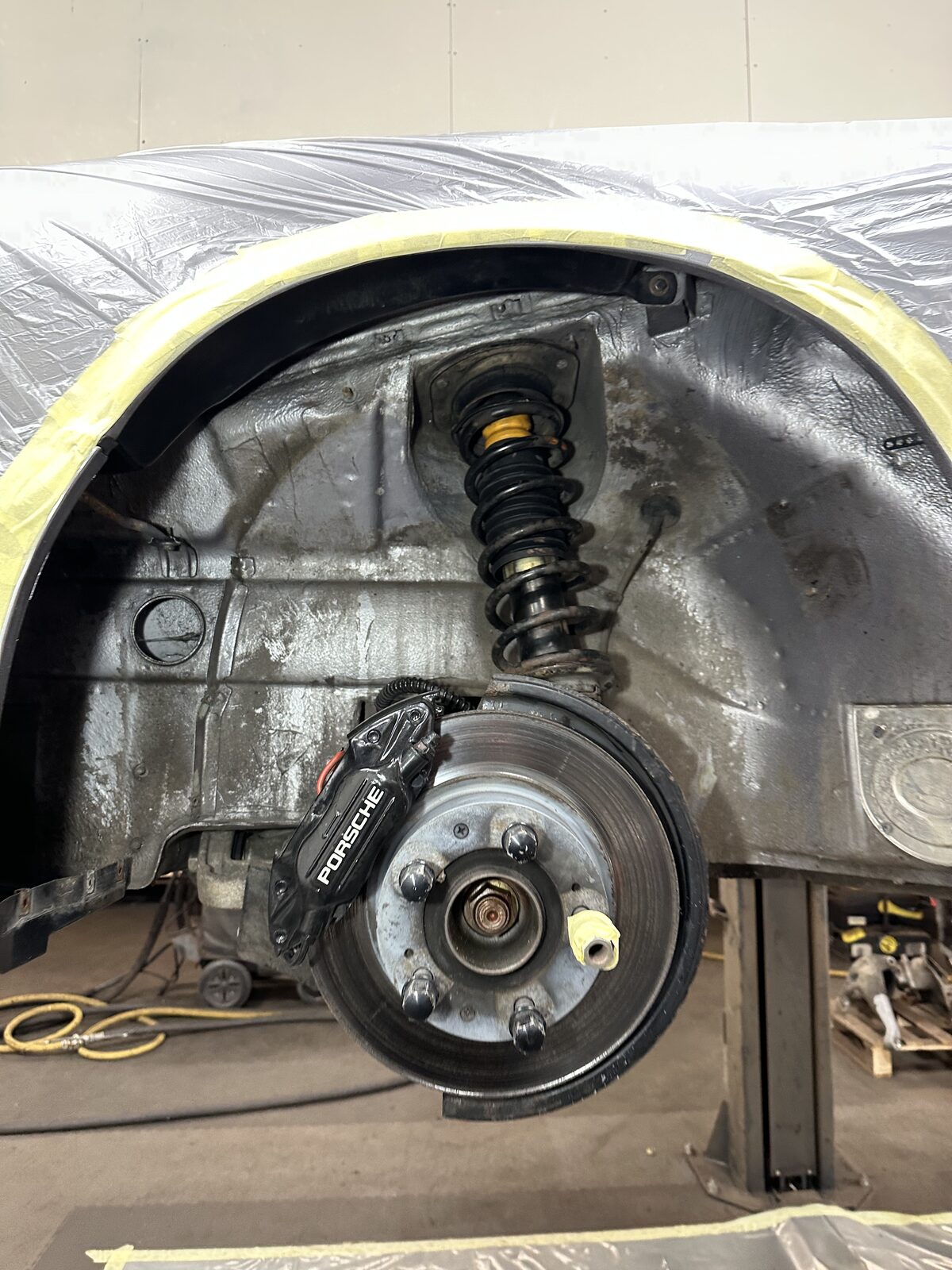 Porsche 911 Carrera 4 rear wheel arch before treatment – coil spring, Porsche brake caliper and a grimy inner arch with the liner removed