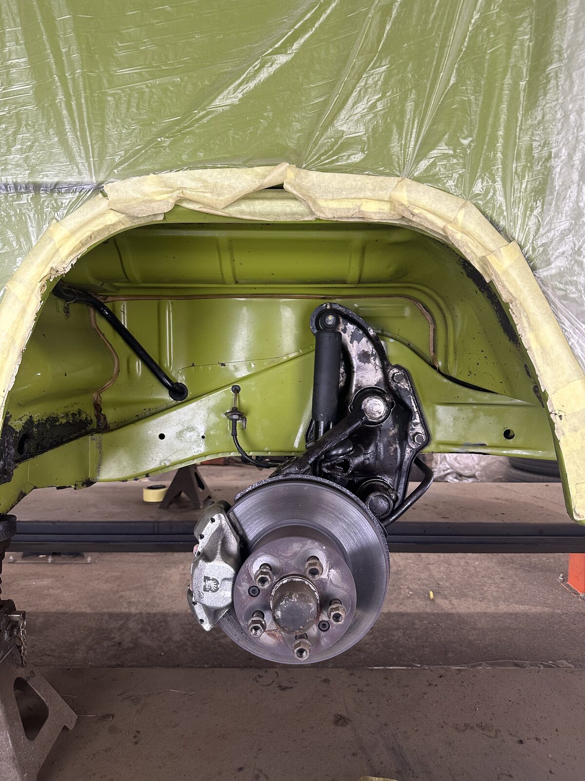 The same Volkswagen T2 camper wheel arch after dry ice underseal removal, cleaned back so the green-painted arch, suspension and hub are exposed for inspection