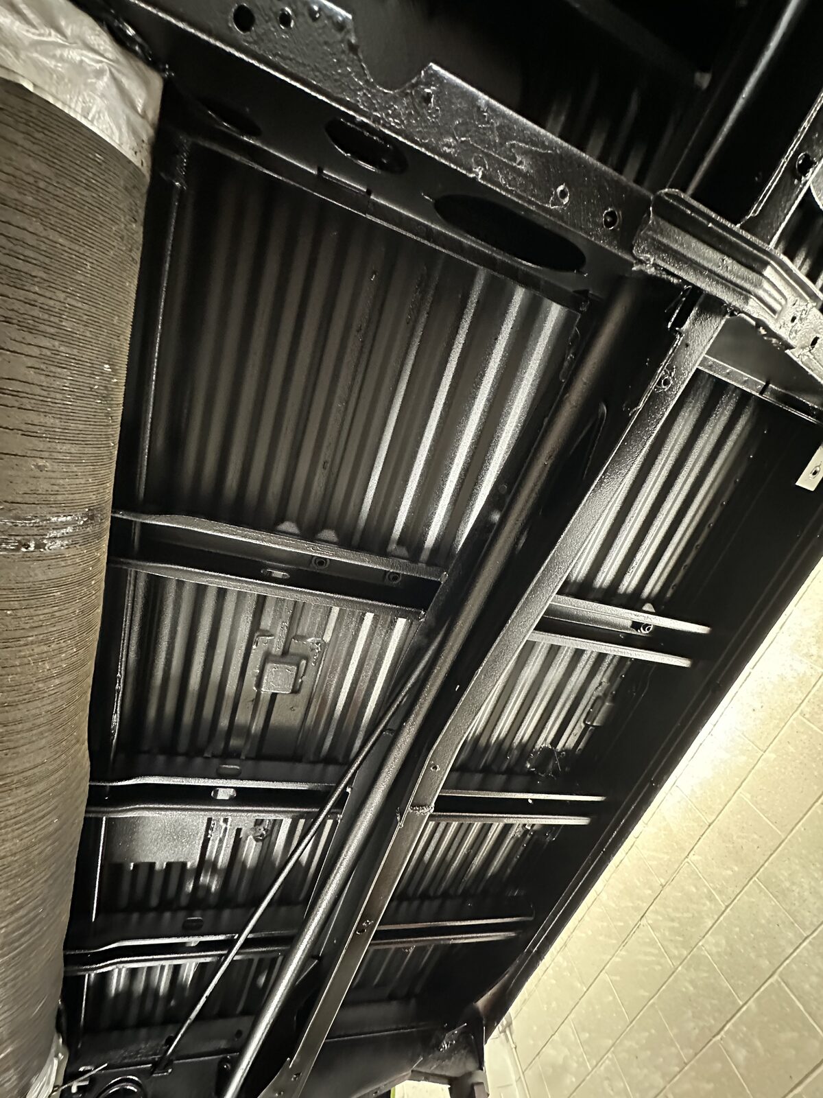 Floor pans, protected – The ribbed floor sections sealed in black, with cavity wax driven into the box sections and rails behind them.